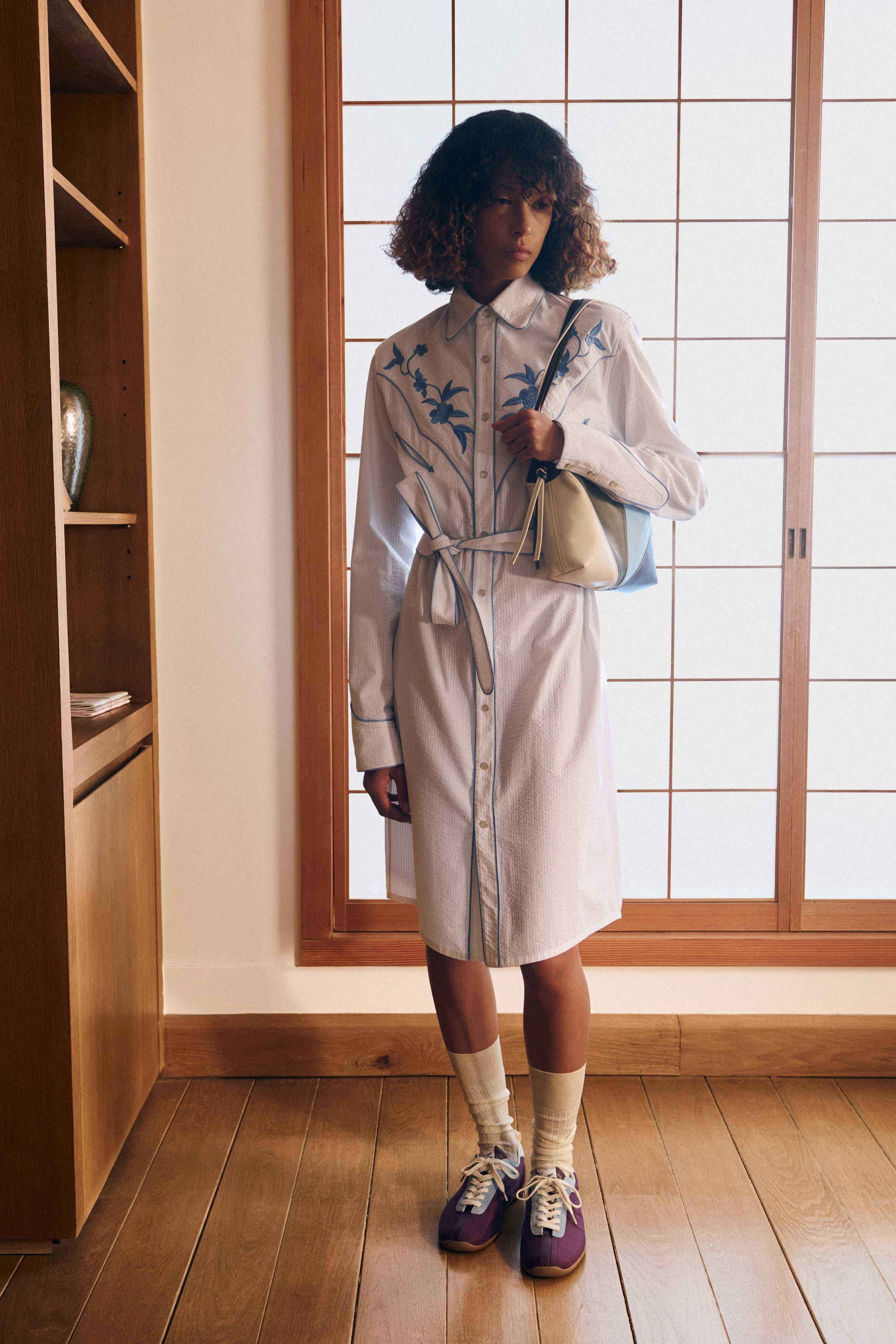 Kenzo 26FW 以“当代旅人”为核心叙事，将日式空间感、巴黎学院派与实穿丹宁重新缝合。剪裁不再强调街头张扬，而是回归比例与层次的节制美学：短外套、羊剪绒飞行夹克、衬衫式连衣廓形在柔光室内场景中显得克制而精准。整体色彩低饱和、结构干净，呈现出一种“被驯化的冒险精神”，让 Kenzo 从符号型街头回到高完成度的现代生活衣橱-顽石频道趋势研究